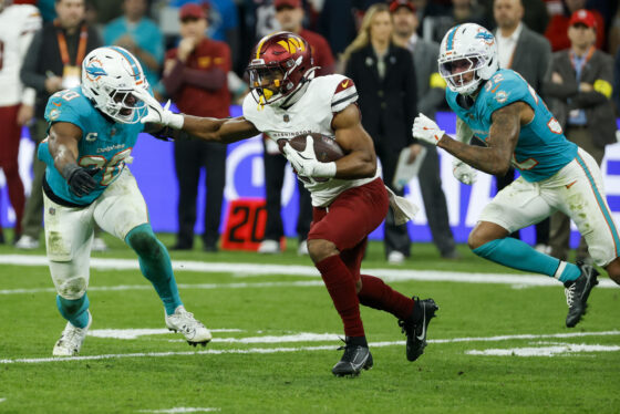 El jugador de los Washington Commanders con el balón ante los jugadores de los Miami Dolphins, durante el partido de liga regular de la Liga de Fútbol Americano (NFL), que este domingo disputan los equipos Miami Dolphins y Washington Commanders, este domingo en el Estadio Santiago Bernabéu. EFE/JuanJo Martín
