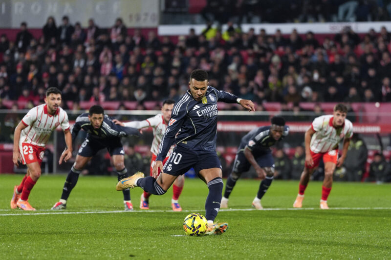 El delantero francés del Real Madrid, Kylian Mbappé, golpea el balón desde el punto de penalti para conseguir el primer gol del equipo madridista durante el encuentro correspondiente a la jornada 14 de Laliga EA Sports que disputaron Girona y Real Madrid en el estadio Montilivi, en Girona. EFE / Siu Wu.