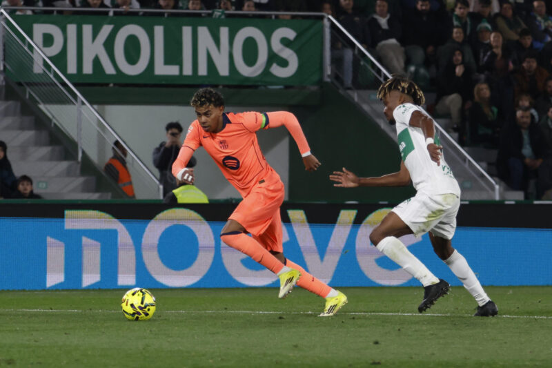 El delantero del FC Barcelona, Lamine Yamal (i), se lleva el balón ante el defensa del Elche, John Donald, durante el encuentro correspondiente a la jornada 22 de la Liga EA Sports que han disputado Elche y FC Barcelona en el estadio Martínez Valero, en la localidad alicantina. EFE / Pablo Miranzo.