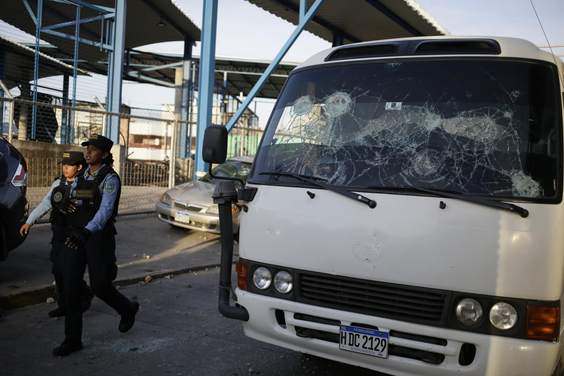 Policías pasan al lado de un vehículo que sufripó daños tras un enfrentamiento entre fanáticos de los equipos Motagua y Olimpia en Tegucigalpa (Honduras). EFE/Gustavo Amador